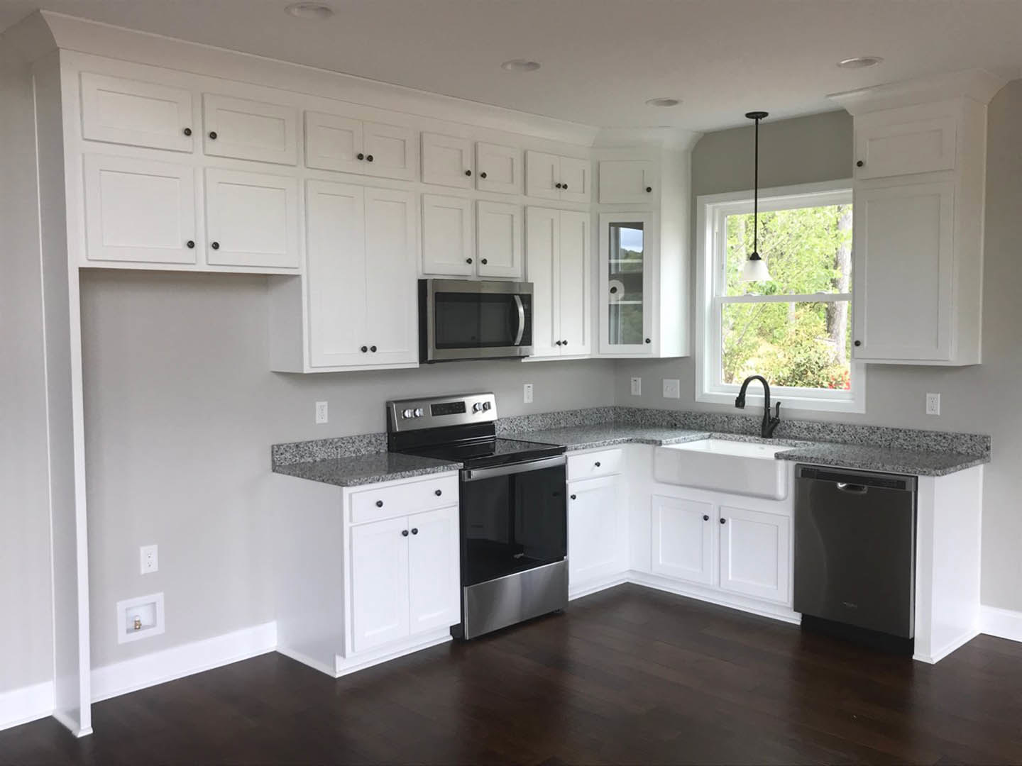 White kitchen cabinets, black appliances including an open microwave and stainless steel oven, light fixture on ceiling, black pole with white stripe, neutral countertops and sink.