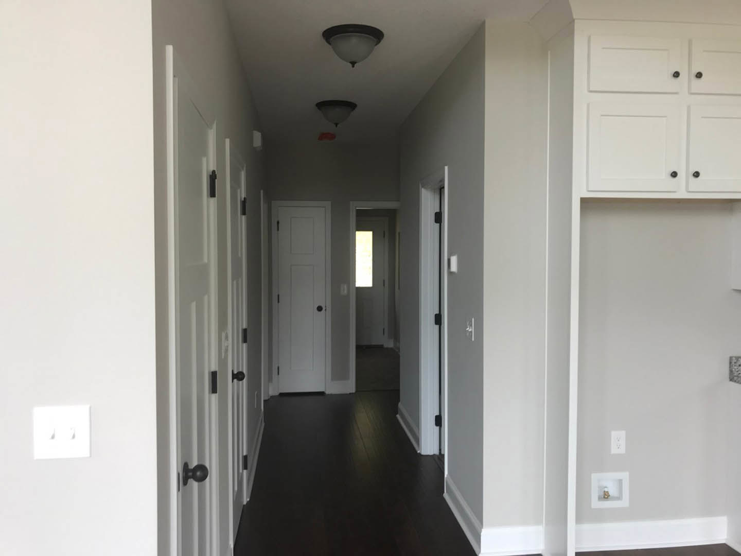 Hallway with white paneled doors, black handles, dark wood flooring, wall-mounted light fixture, white cabinet with black knobs