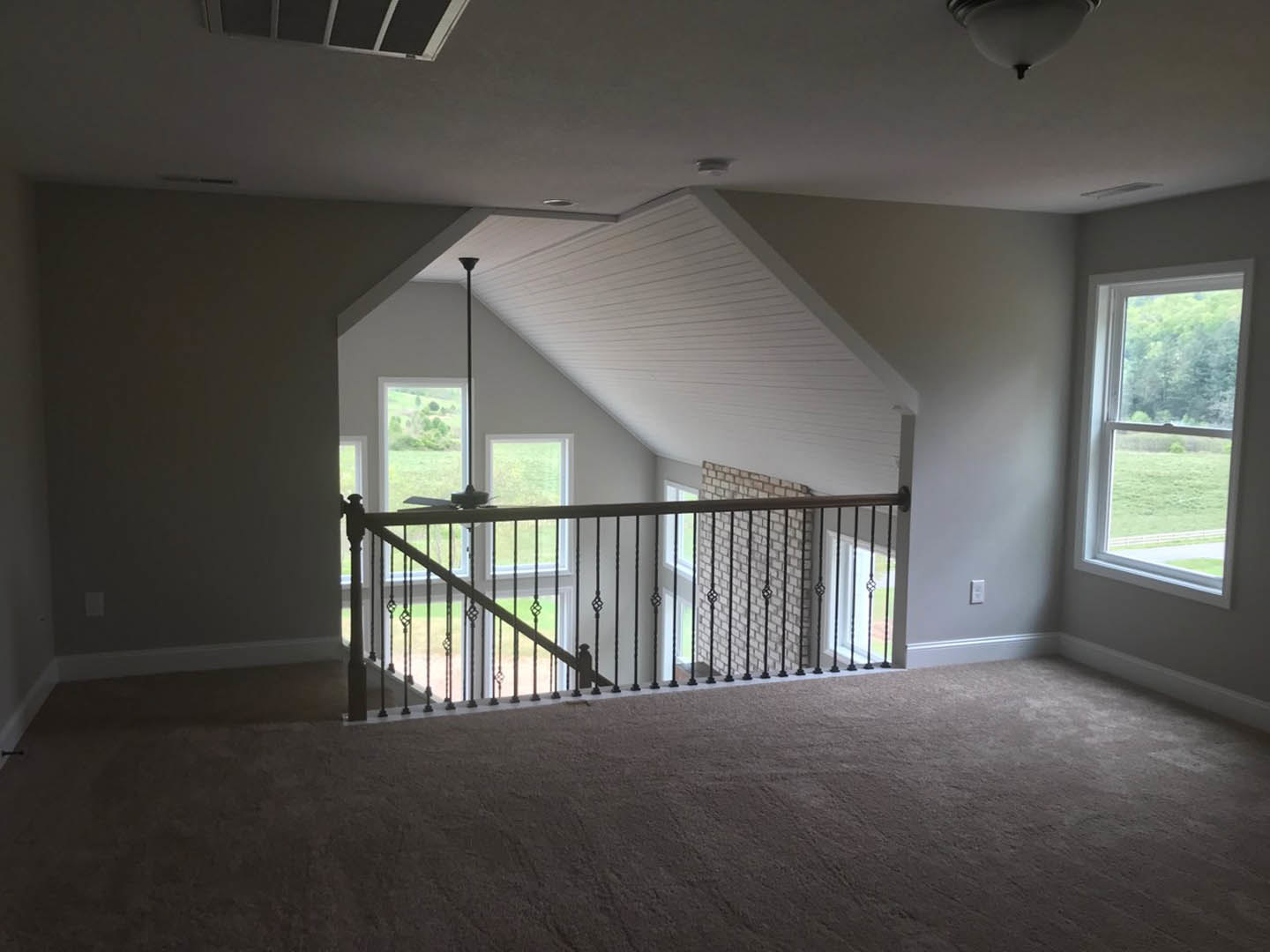 Staircase with wooden railing, carpeted floor, large window overlooking trees, recessed ceiling light, smooth plaster walls