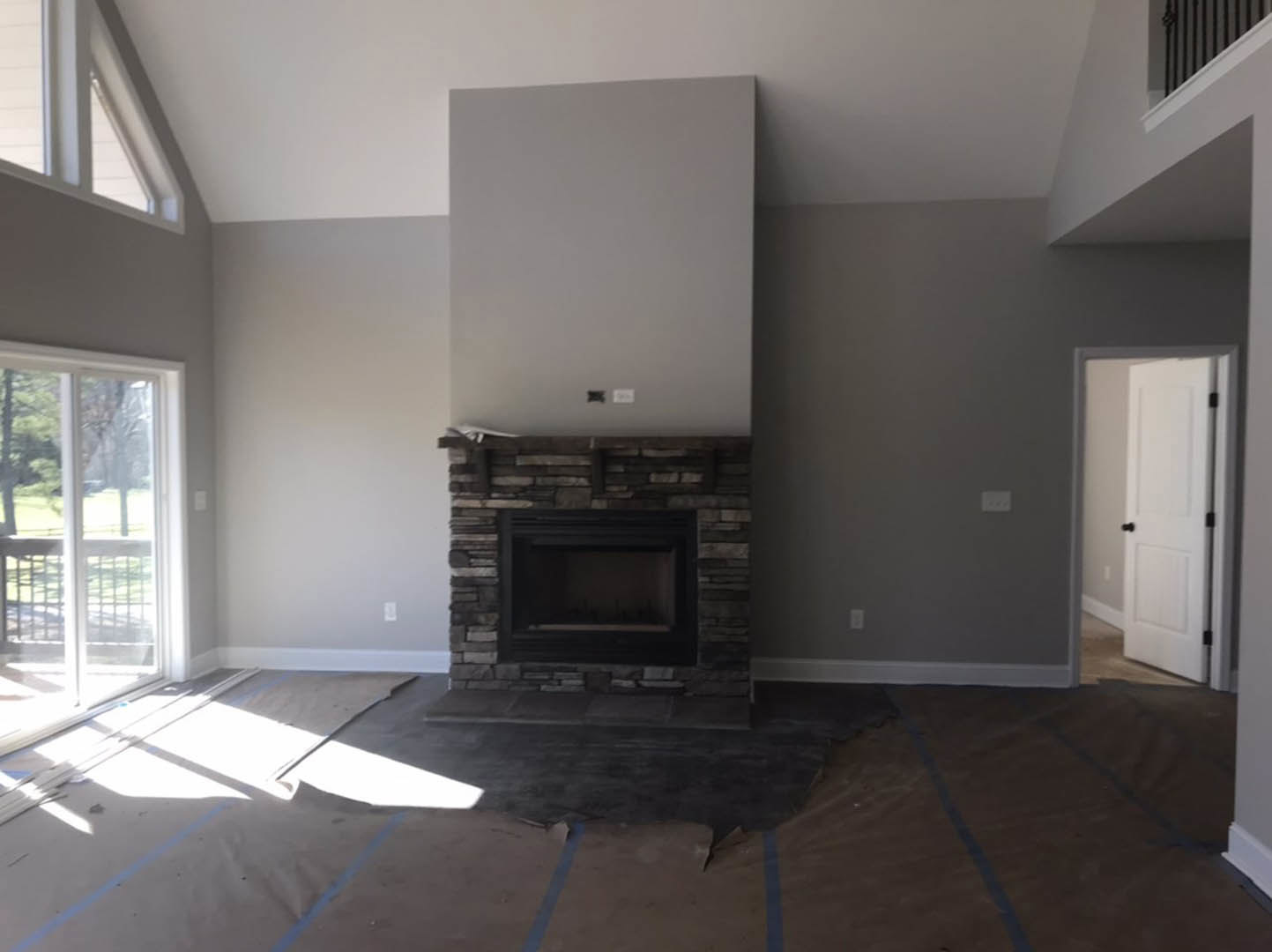 Modern living room with wood laminate flooring, white fireplace, large window with sheer white curtain, white door with black hardware, and recessed lighting illuminating the space