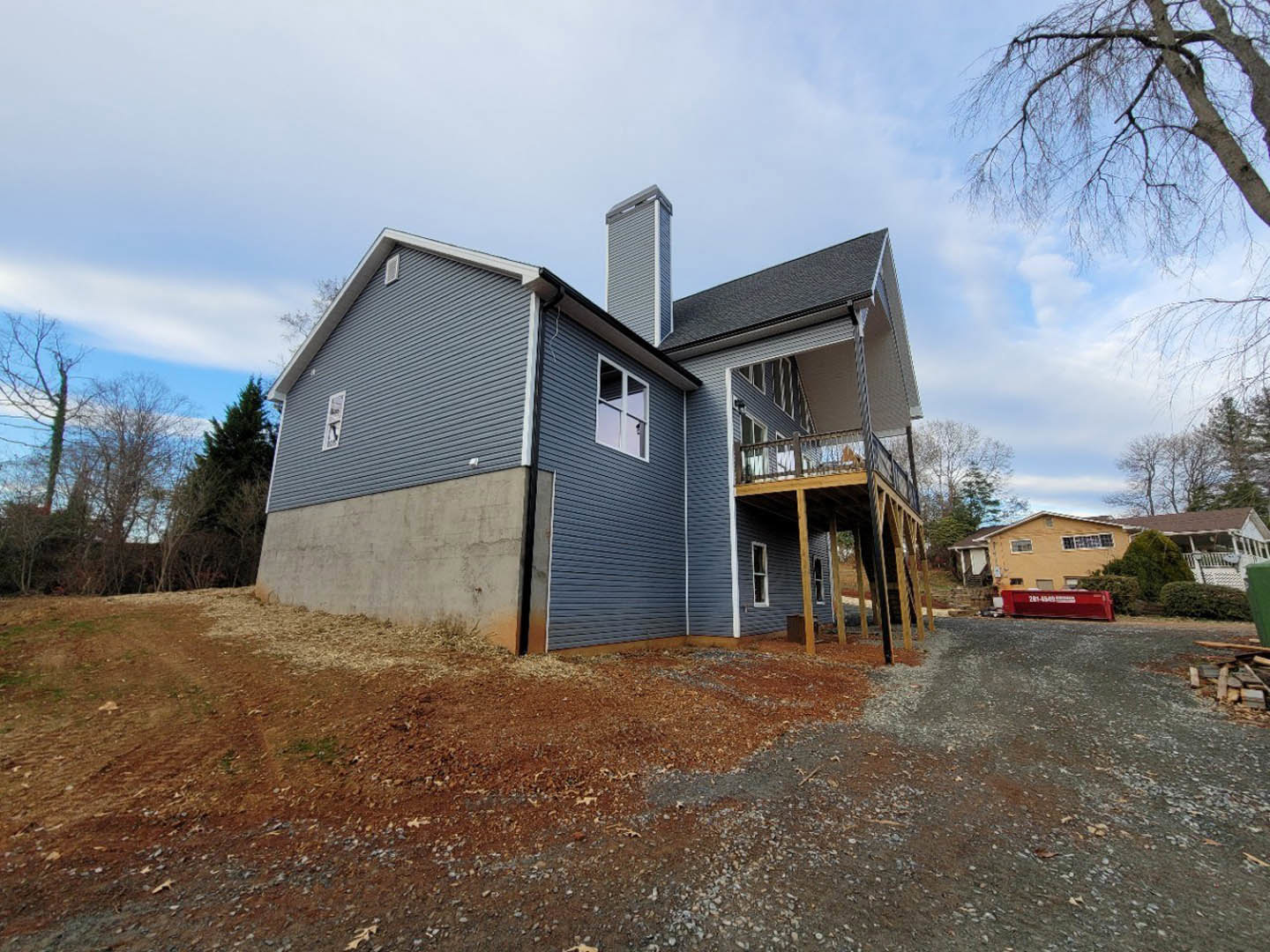 Two-story house with covered front porch, multi-pane windows, balcony above garage, brick chimney, attached garage door, concrete driveway, landscaped yard with trees and shrubs