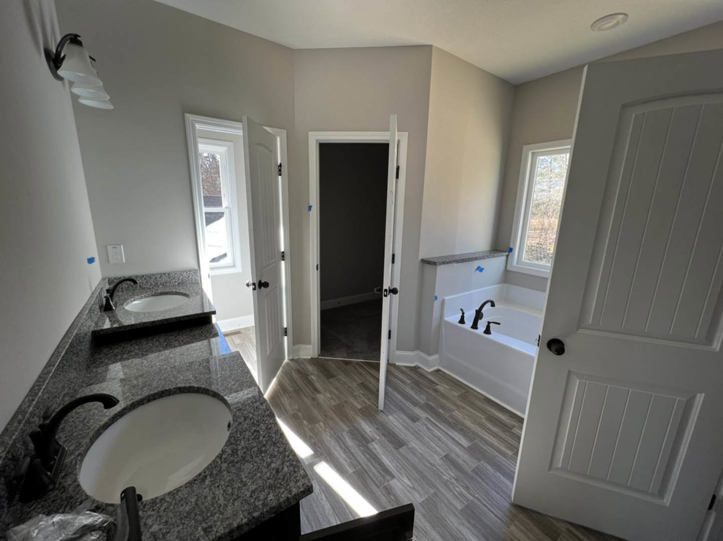 Bathroom with marble countertop, undermount sink, freestanding bathtub, white door with black handle, wall-mounted light fixture, tile flooring, and large mirror