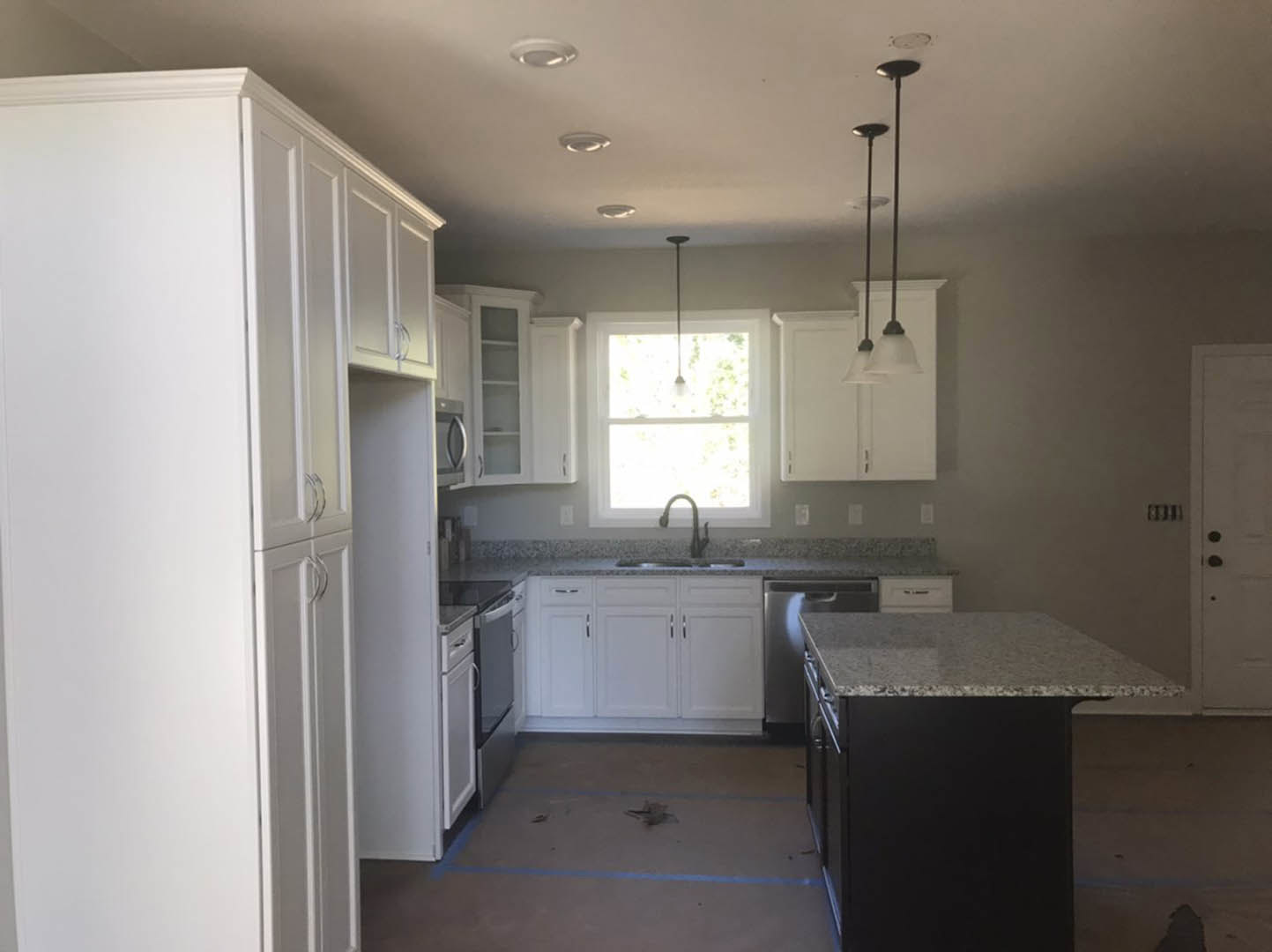 White kitchen with granite countertops, central island, window above sink, silver cabinet handles, and pendant light fixture
