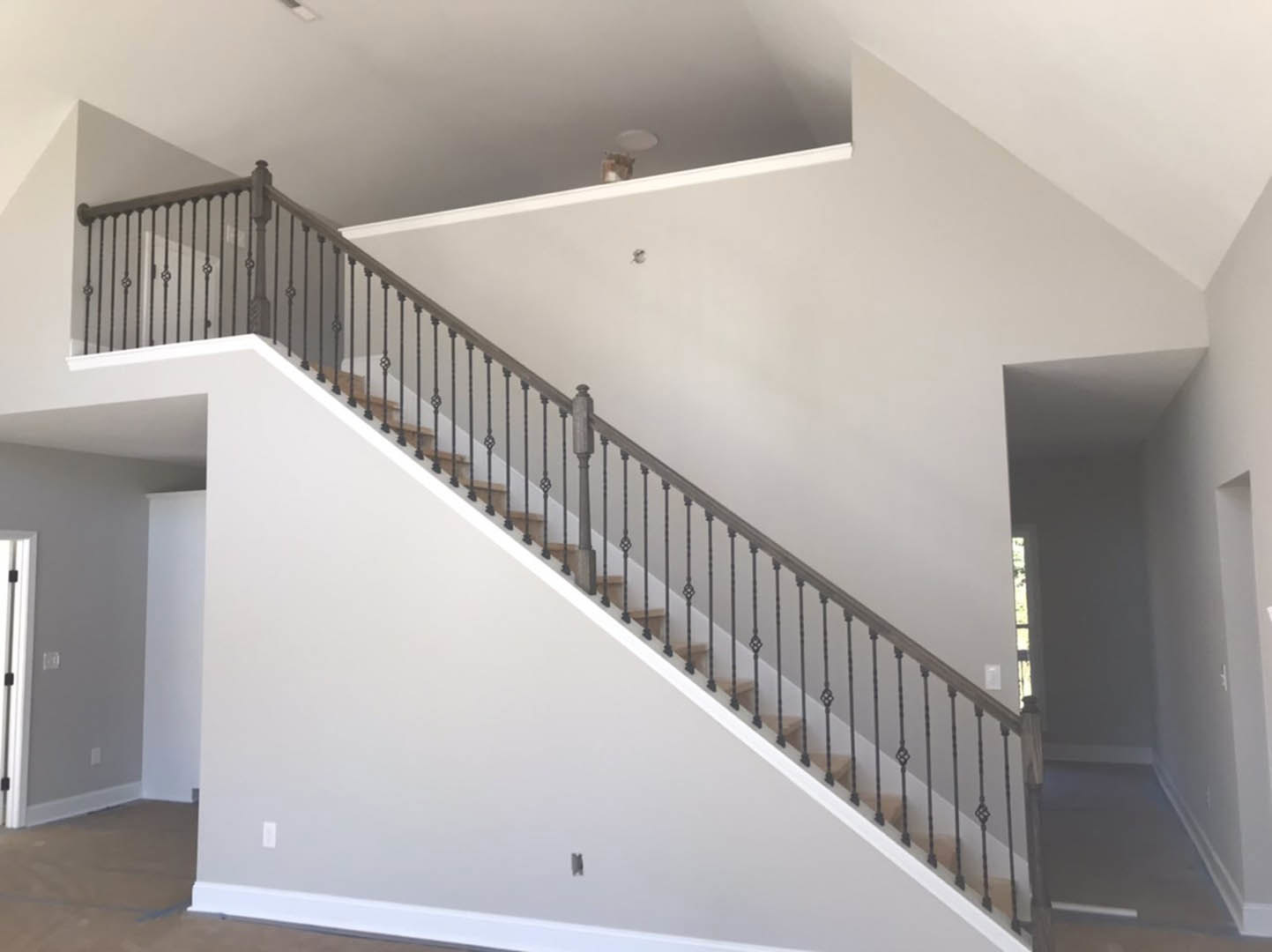 Wood staircase with black metal railings, white plaster walls, light hardwood floors, and recessed ceiling lighting