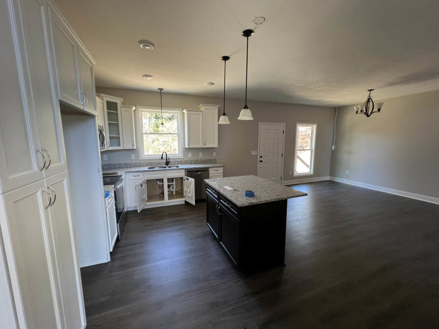 Kitchen with central island featuring blue tape on white countertop, stainless steel sink, white cabinetry, black hardware, window with white frame, and light wood flooring.