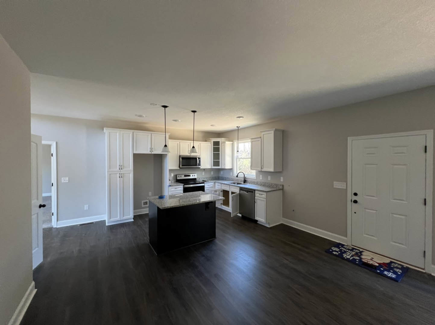 Open kitchen and dining area featuring white cabinetry, black marble countertop, white door with black handles, built-in microwave with black screen, and silver oven; laminate wood