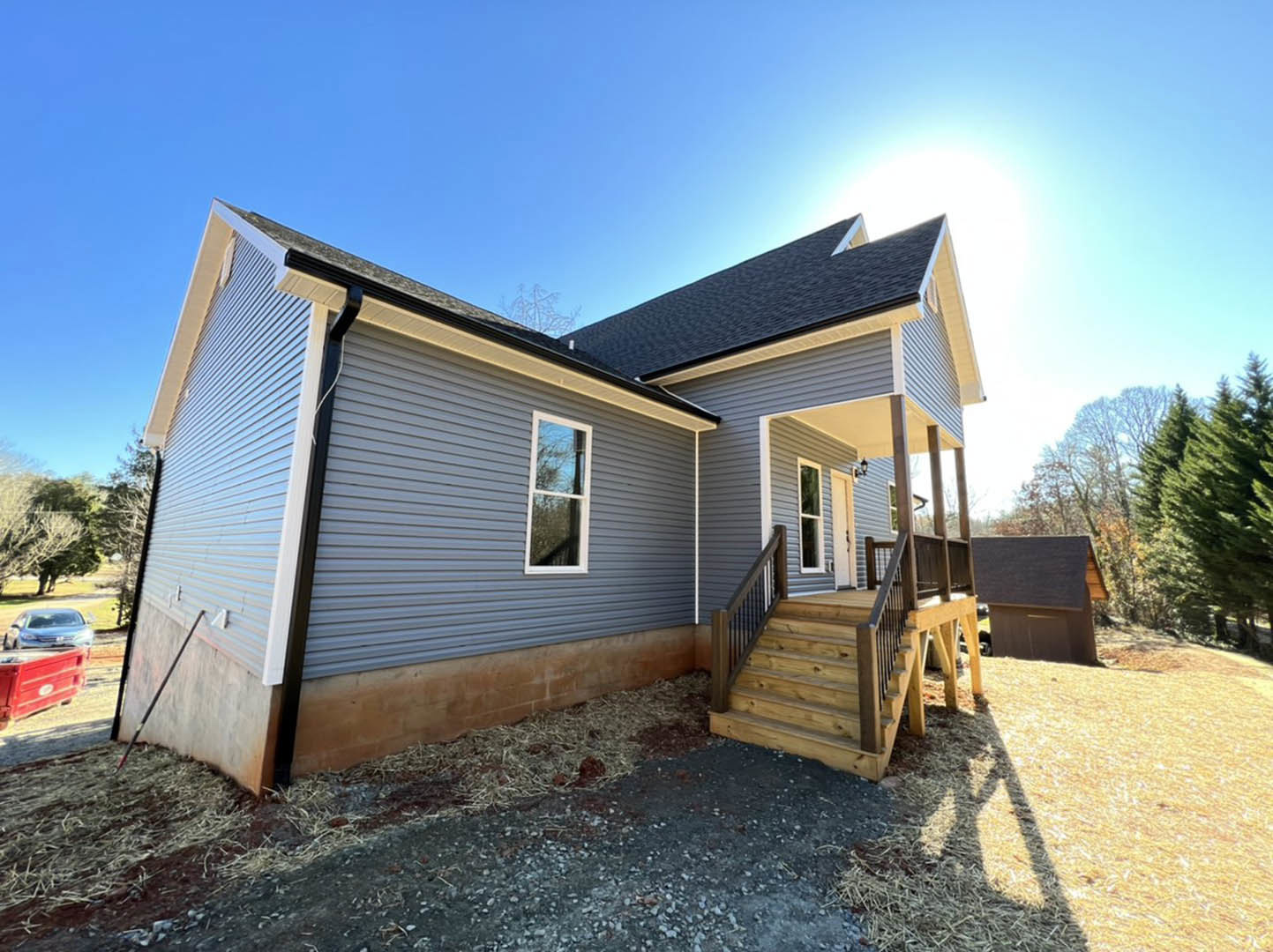 Two-story house with white-framed windows, covered front porch, driveway, exterior staircase, red dumpster near garage, car and tree partially visible in foreground