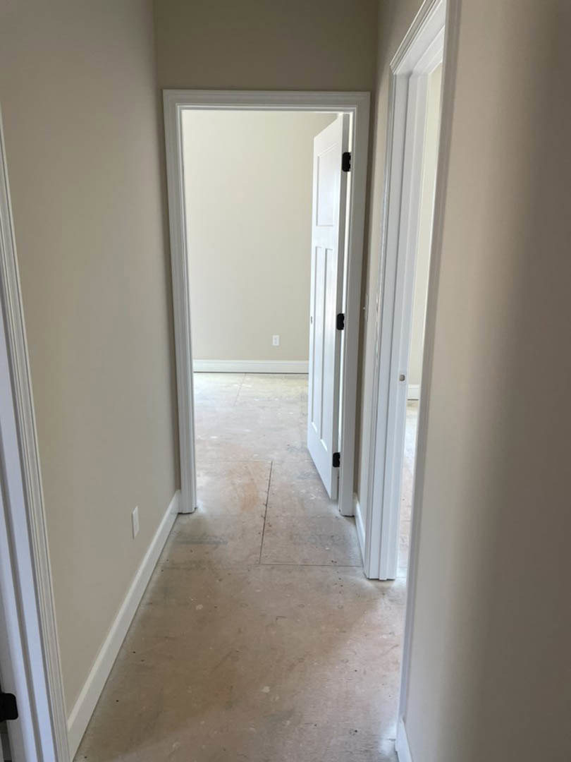 Hallway with white paneled doors, black handles and hinges, light tile flooring, and smooth white plaster walls