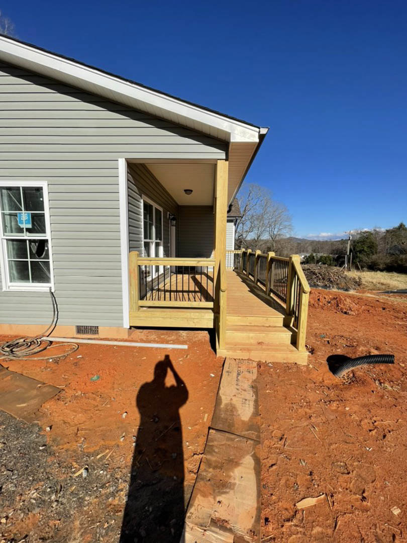 Modern home exterior with light siding, large windows, and covered porch; sunlight casts a person's shadow across the paved ground.