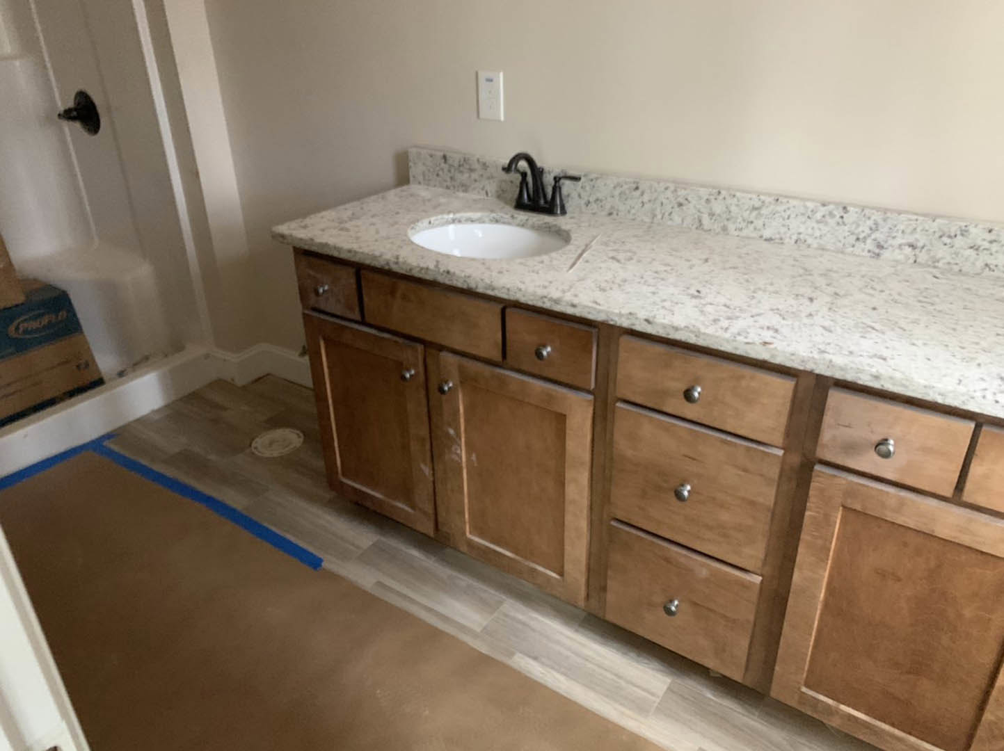 Bathroom with light wood cabinets, white countertop, black faucet, and tile backsplash
