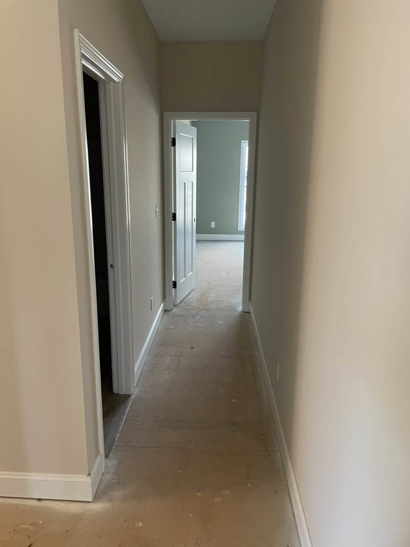 White hallway with white trim and plaster walls, open white door, light fixture on wall, hardwood flooring