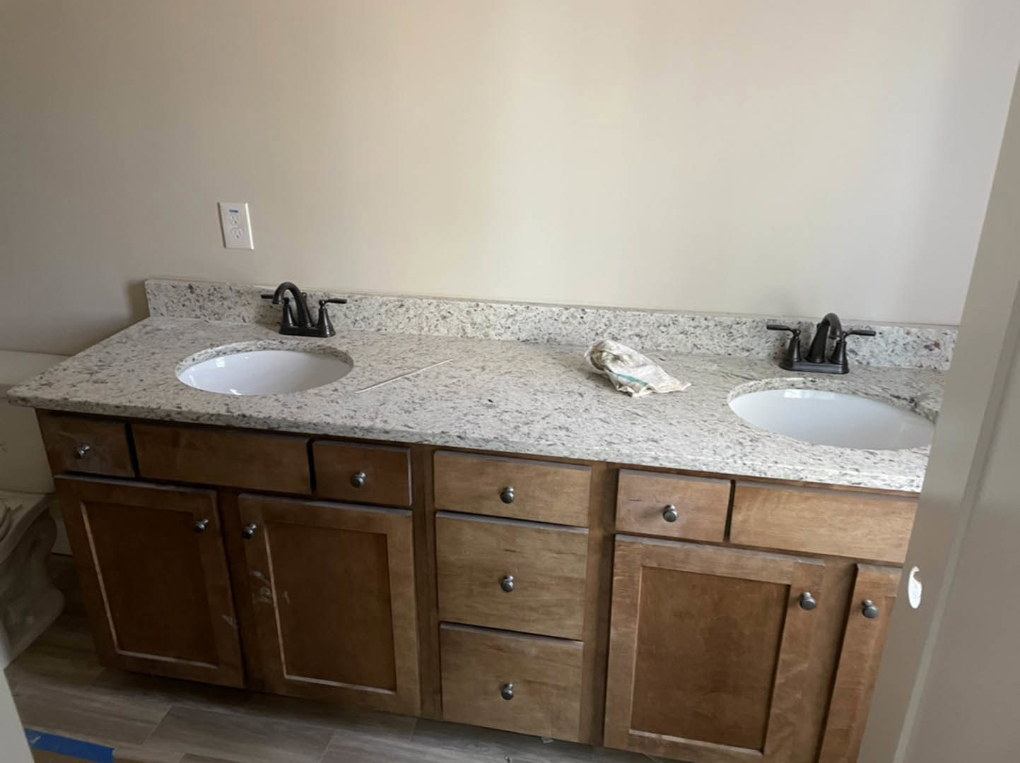 Double vanity bathroom with light wood cabinets, white countertop, chrome faucets, tile backsplash, and wall outlet