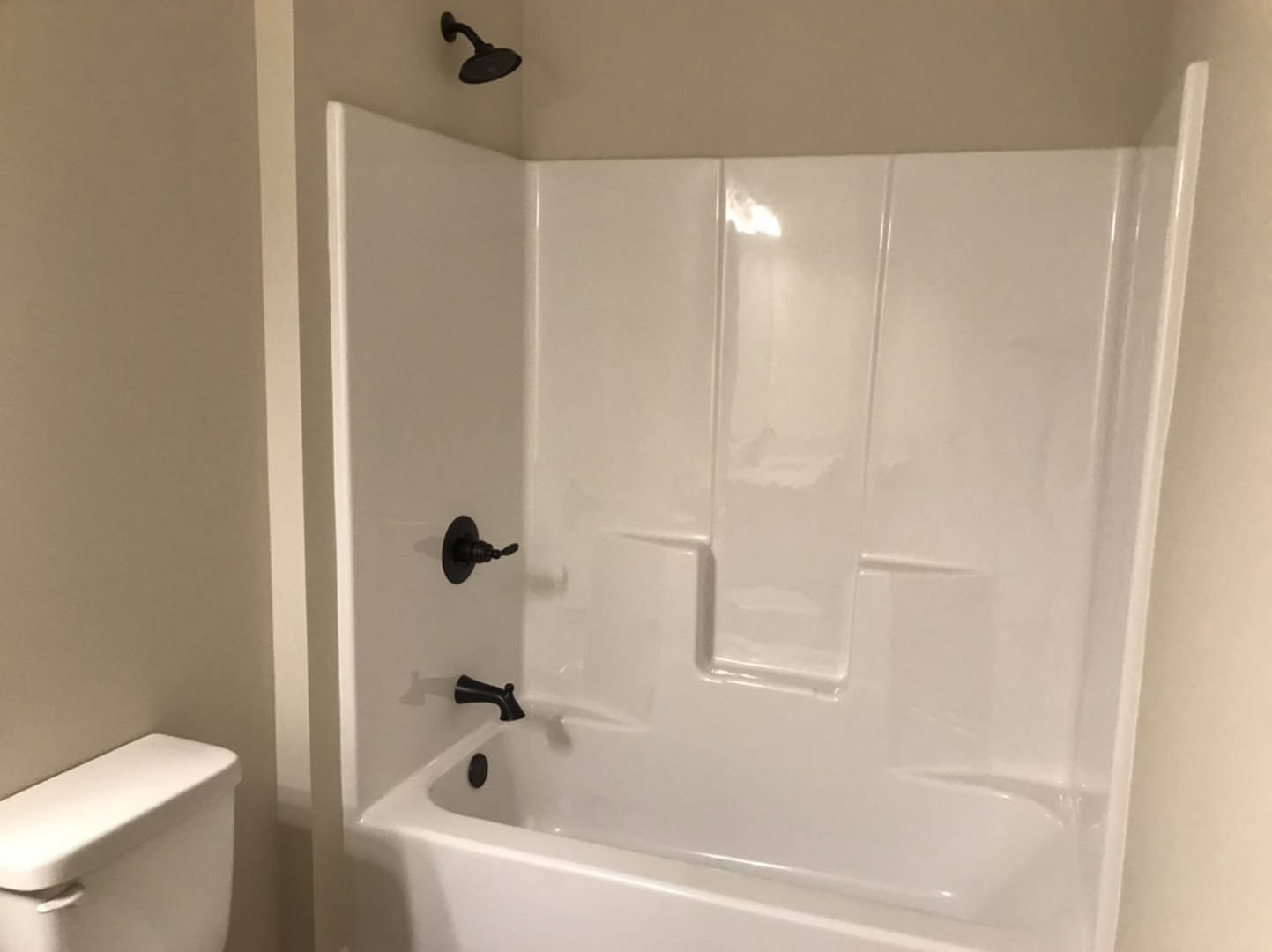 Freestanding white bathtub with matte black fixtures beside white toilet, surrounded by light tile walls and floor, shower head mounted on wall