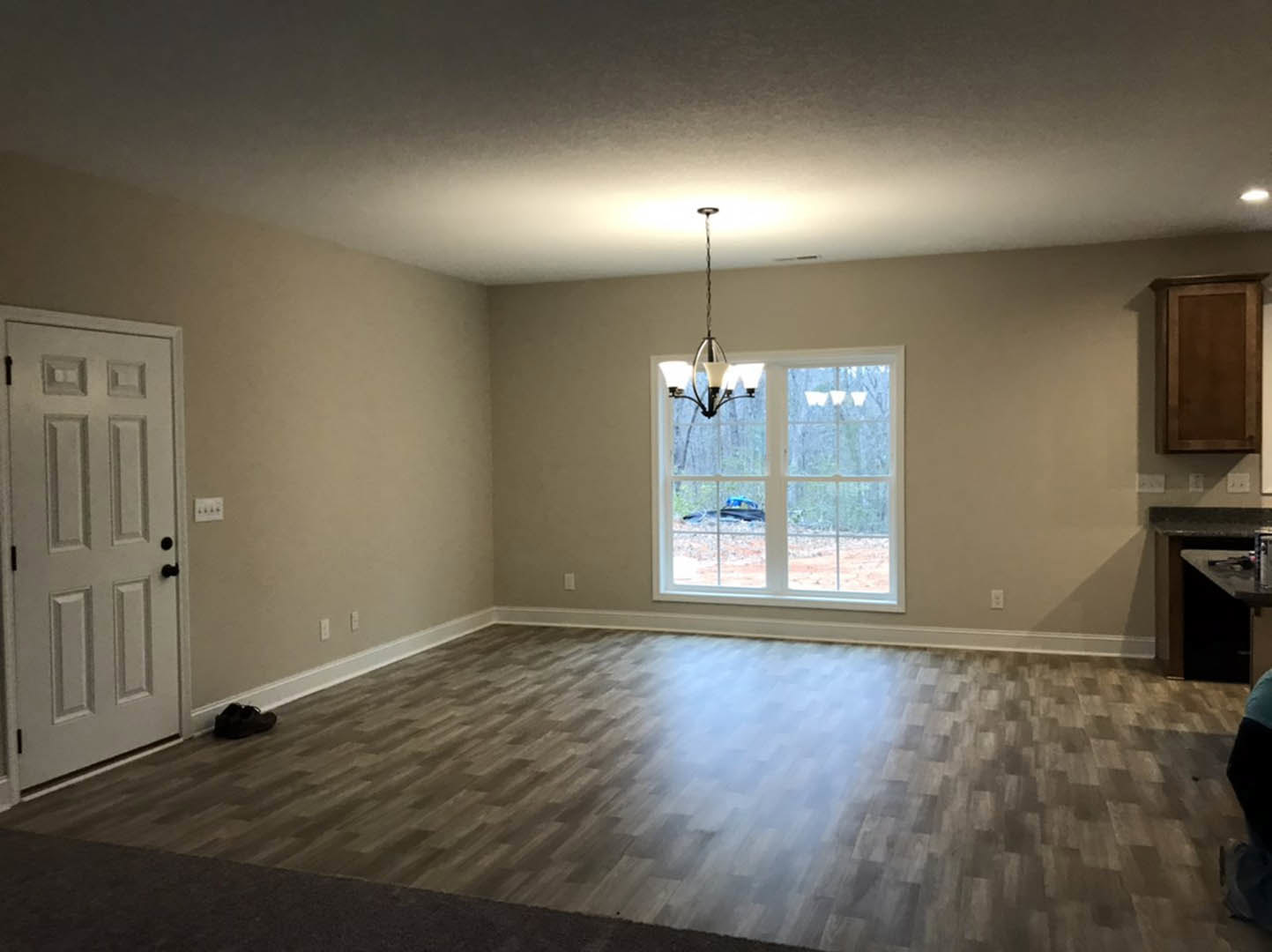 Wood floor room with white door featuring black handles, window showing parked car outside, brown rectangular object with white border, chandelier overhead, and black shoe on