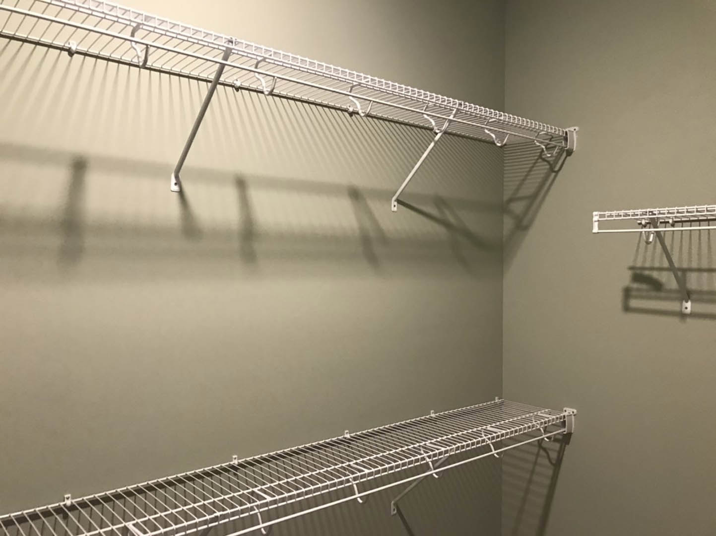 White built-in shelving unit with metal rod and hooks mounted on a wall in a room, casting shadows on the white surface.