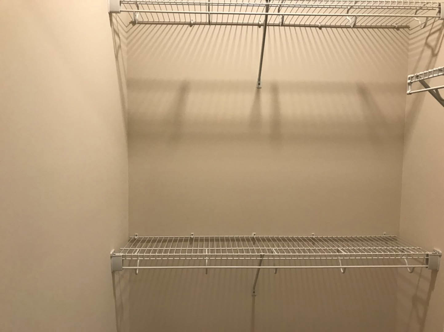 White wire shelving mounted on a wall above a white toilet tank with chrome handle in a small indoor room.
