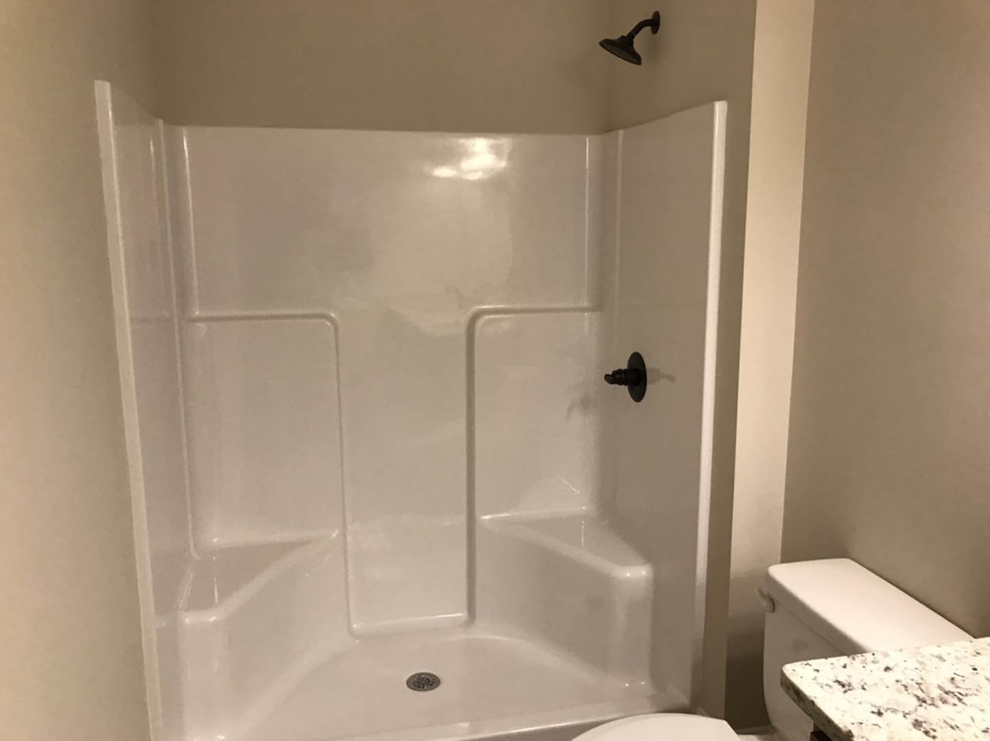 White tile shower with chrome showerhead, marble countertop beside toilet, black wall-mounted fixture, and floor drain