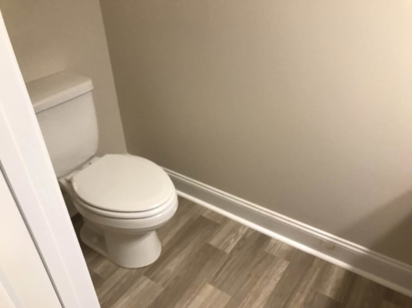 White toilet with closed lid on wood floor, white wall and baseboard in bathroom