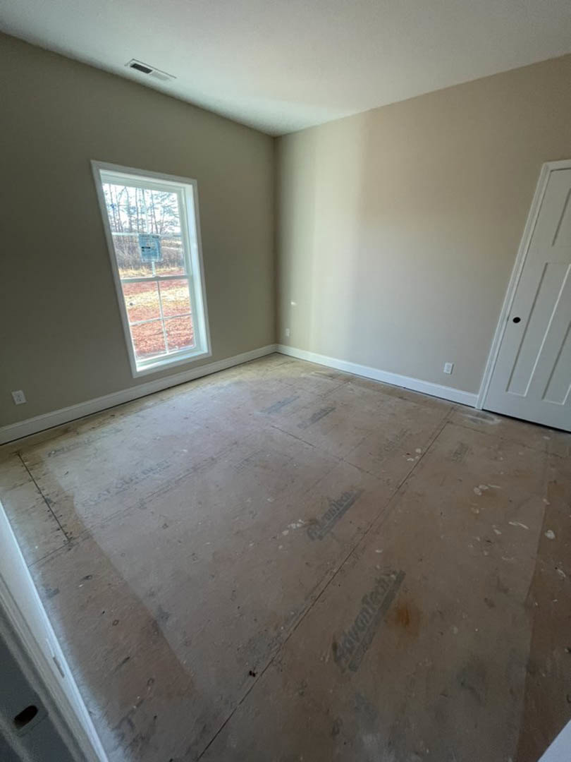 Room with white plaster walls, tile flooring, large window, and white door; ceiling corner visible, window features a sign, door has a hole near handle.