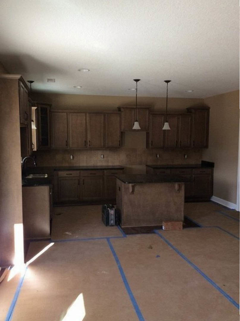 Kitchen with brown wood cabinetry, black countertop, tile flooring, ceiling fan, and blue painter’s tape on the floor near a pillar.