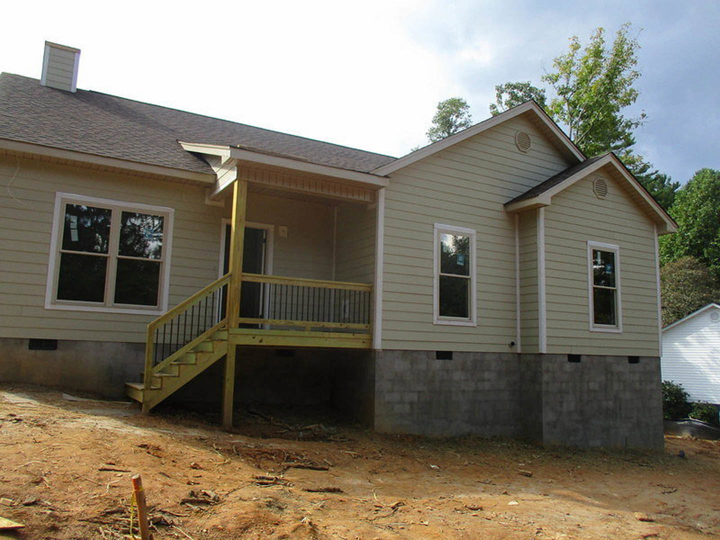 White house with red roof, wooden porch and stairs, white-framed windows, railing along deck, close-up of exterior wall, window with sign, trees and sky in background