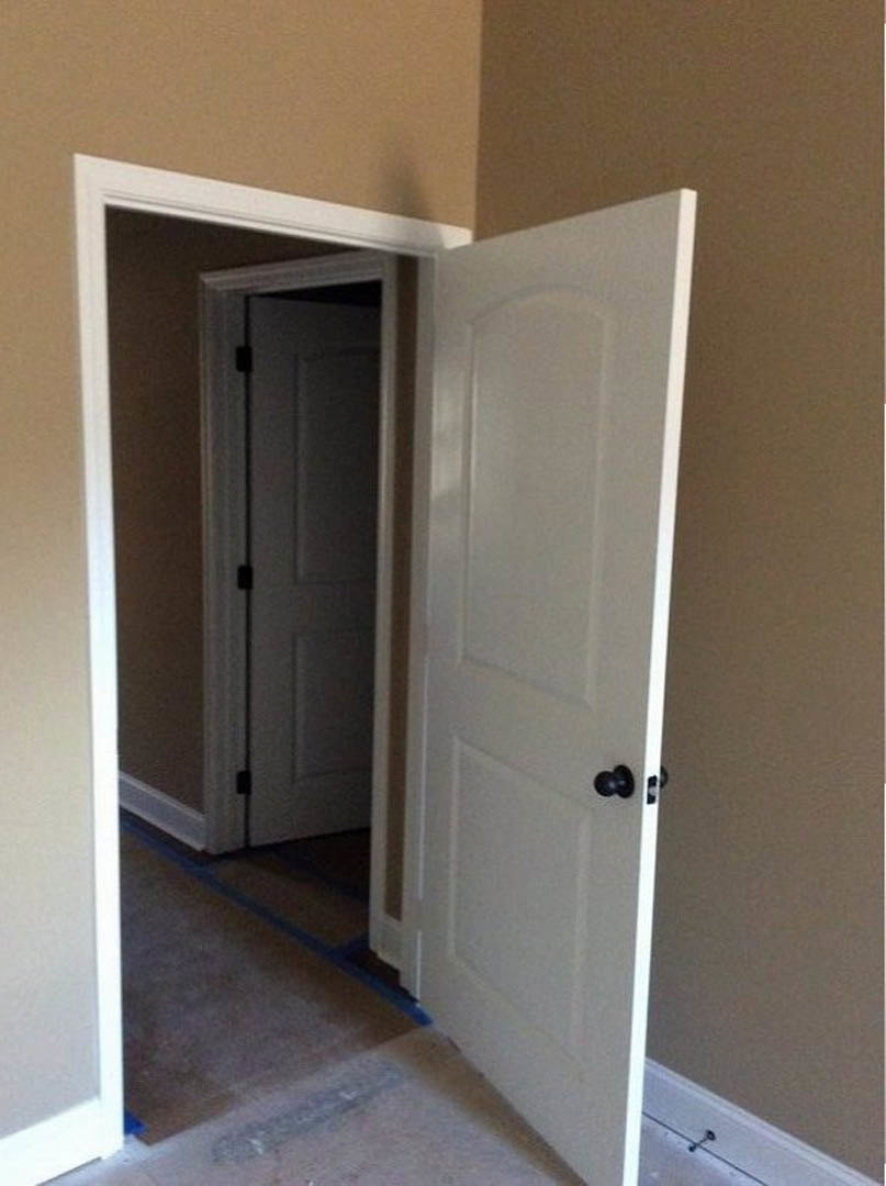 White paneled door with black knob open to reveal carpeted hallway, neutral walls, and baseboard trim