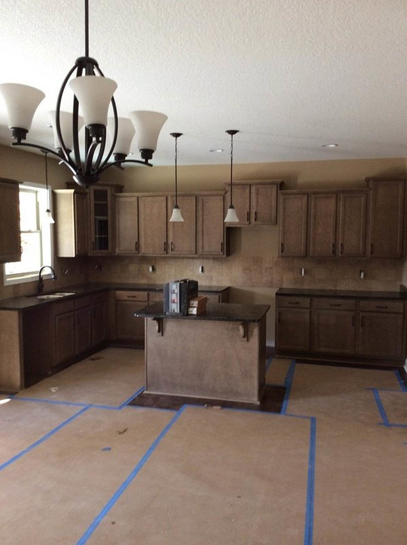 Bright kitchen featuring a central island with stone countertop, elegant chandelier overhead, white cabinetry, tile backsplash, stainless steel sink, and hardwood flooring.