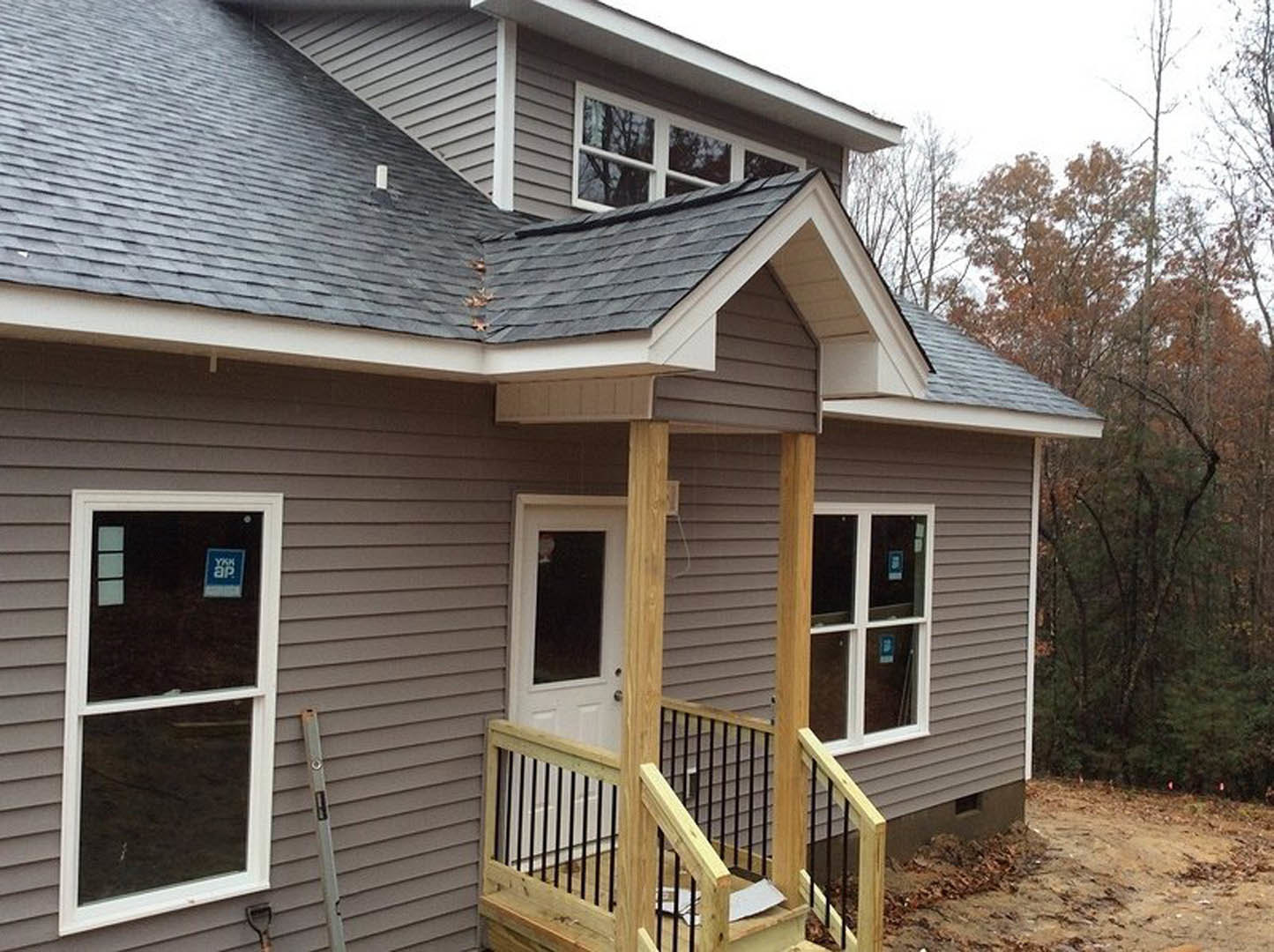 Two-story home with light siding, covered porch featuring wooden railing, white-framed windows, and front stairs leading to entry