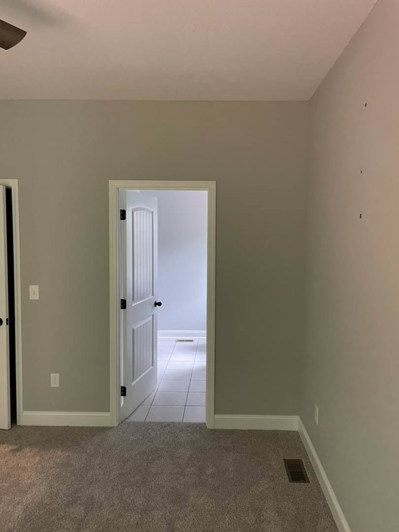 White paneled door with black knob, white baseboard molding, carpeted floor, and rectangular floor vent
