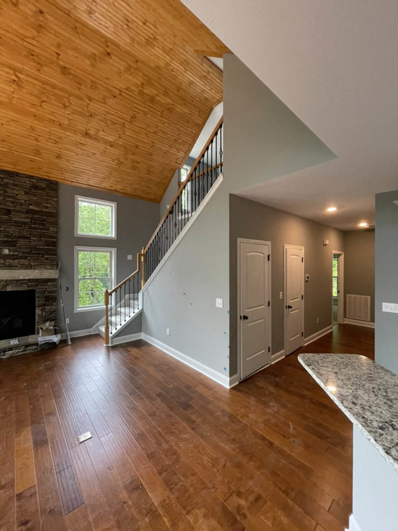 Living room with hardwood floors, wood ceiling, white walls, built-in fireplace, and white door with black hardware
