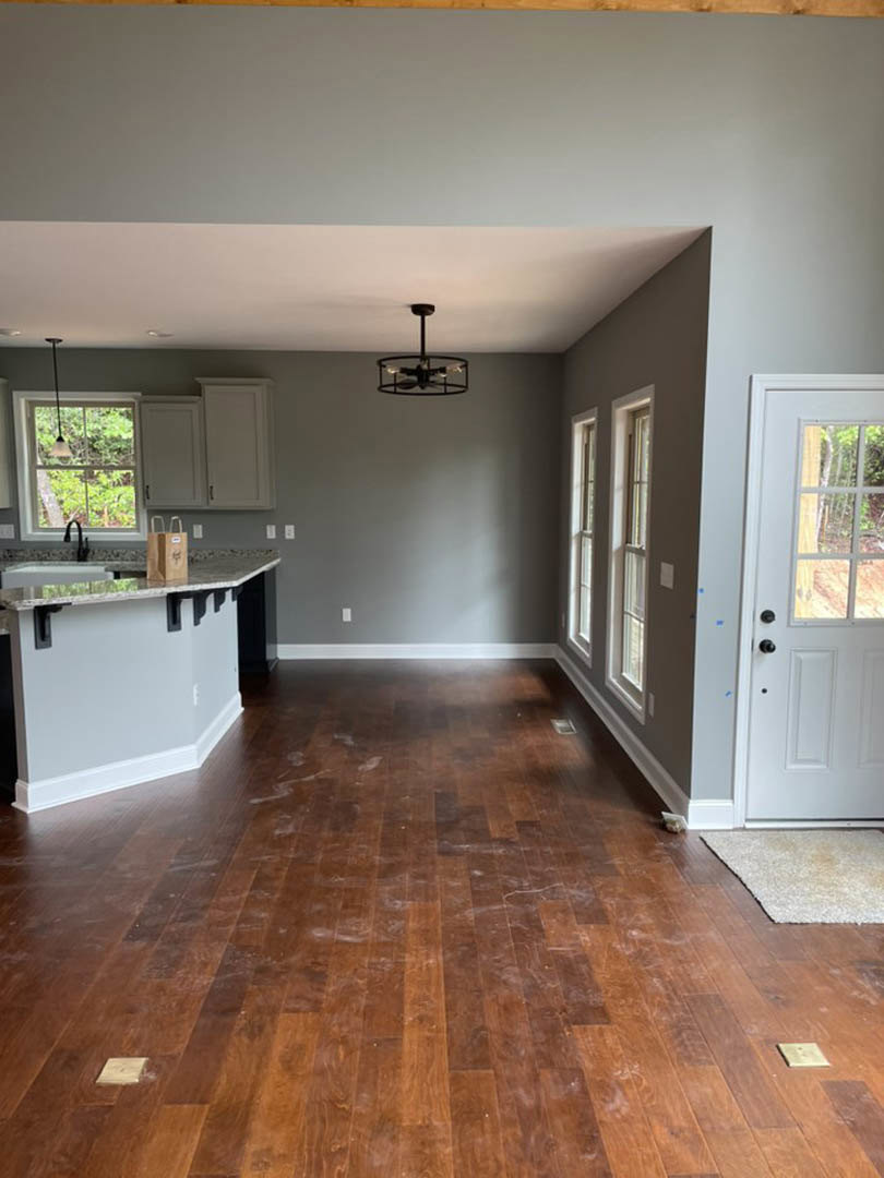Open kitchen and dining area featuring hardwood floors, white walls, large windows, glass-paneled door, ceiling light fixture, and a brown bag resting on the countertop.