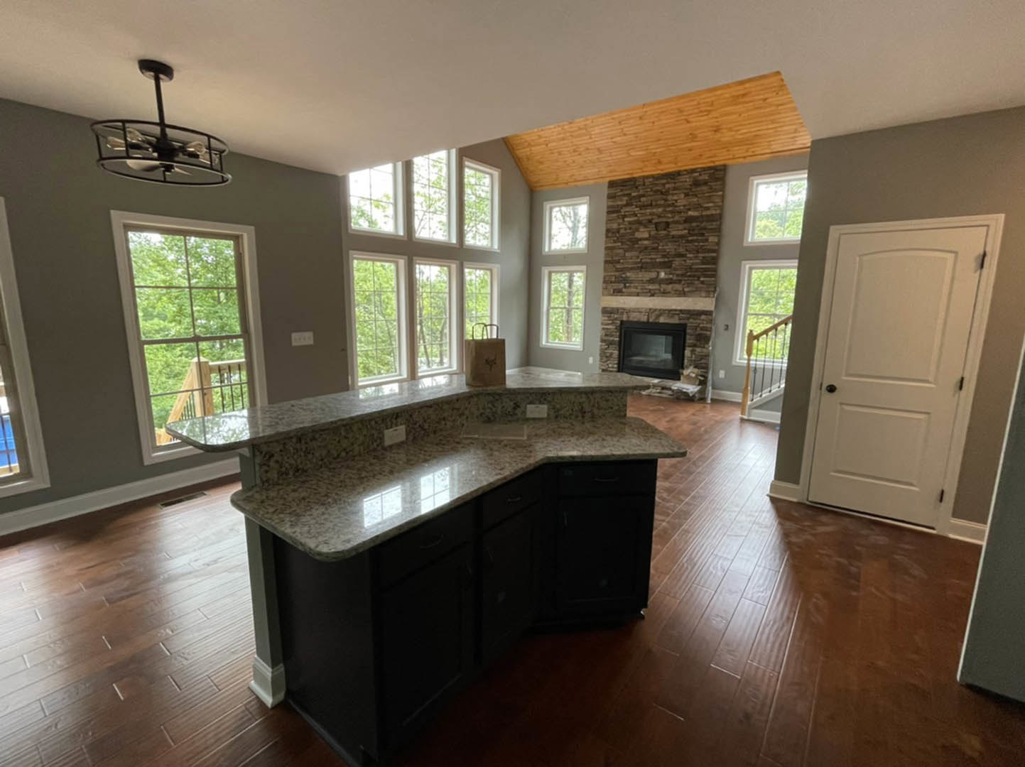 Kitchen featuring central black fireplace with glass window, marble-topped island, white cabinetry with black knobs, wood-paneled accent wall, tile flooring, ceiling fan with light