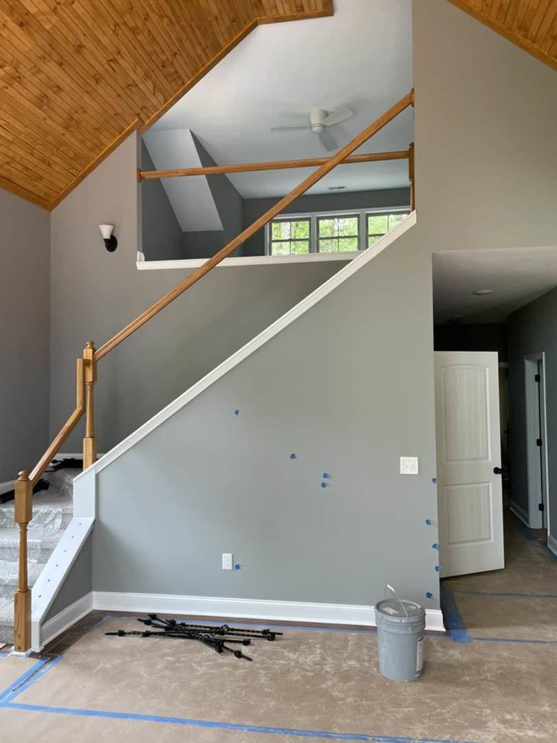 Wood staircase with dark handrail, white walls, white door with black handle, light grey flooring, and white ceiling fan in modern interior.