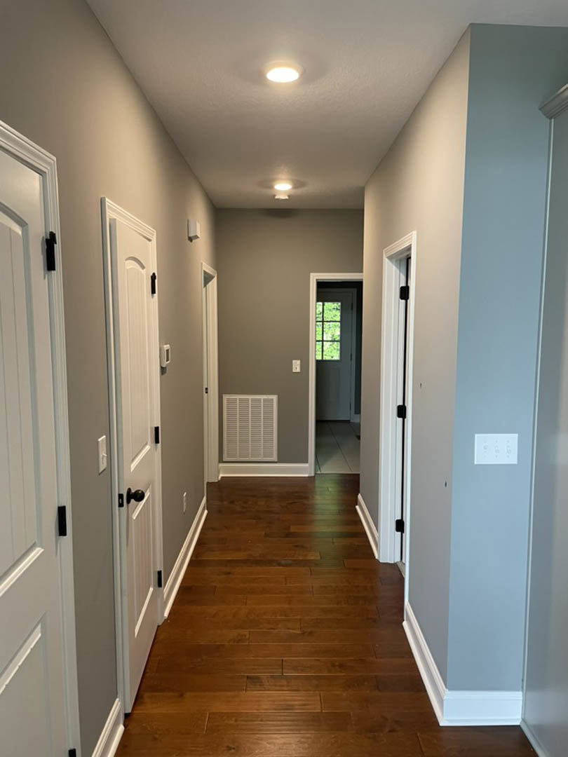 Hallway with white paneled doors, light hardwood flooring, wall vent, window, and light switch on neutral painted walls