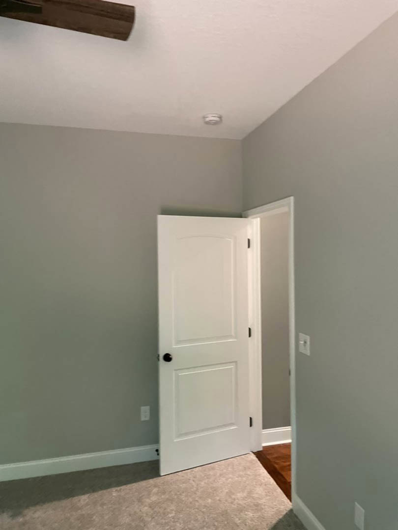 White paneled door with black handle set in a light-colored plaster wall, hardwood flooring, and partial view of a wooden table in foreground