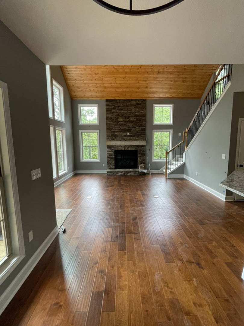 Living room with stone fireplace, hardwood floors, staircase with metal railing, white door with black handle, recessed ceiling lights
