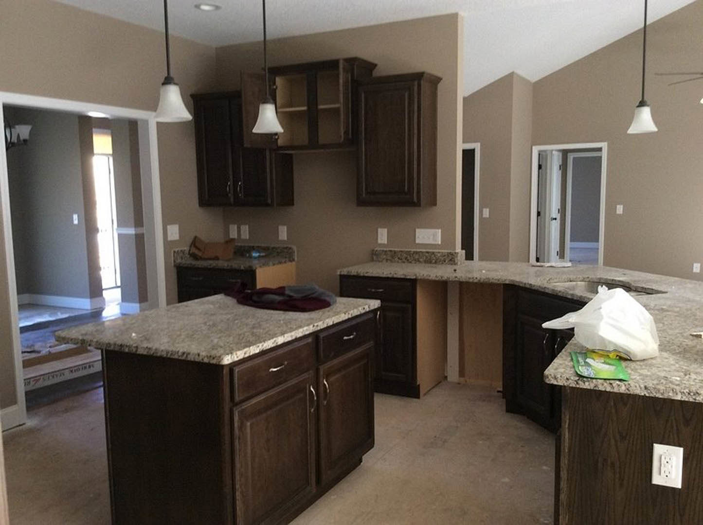 Kitchen with granite countertops, white cabinetry, kitchen island, stainless steel sink, white outlet, plastic bag on counter, partial view of a door, blurry feet visible on floor