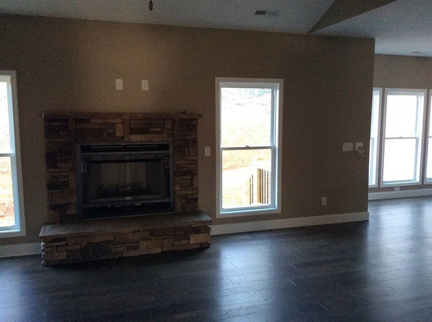 Stone fireplace with white-framed window, wood flooring, and neutral walls in a cozy den