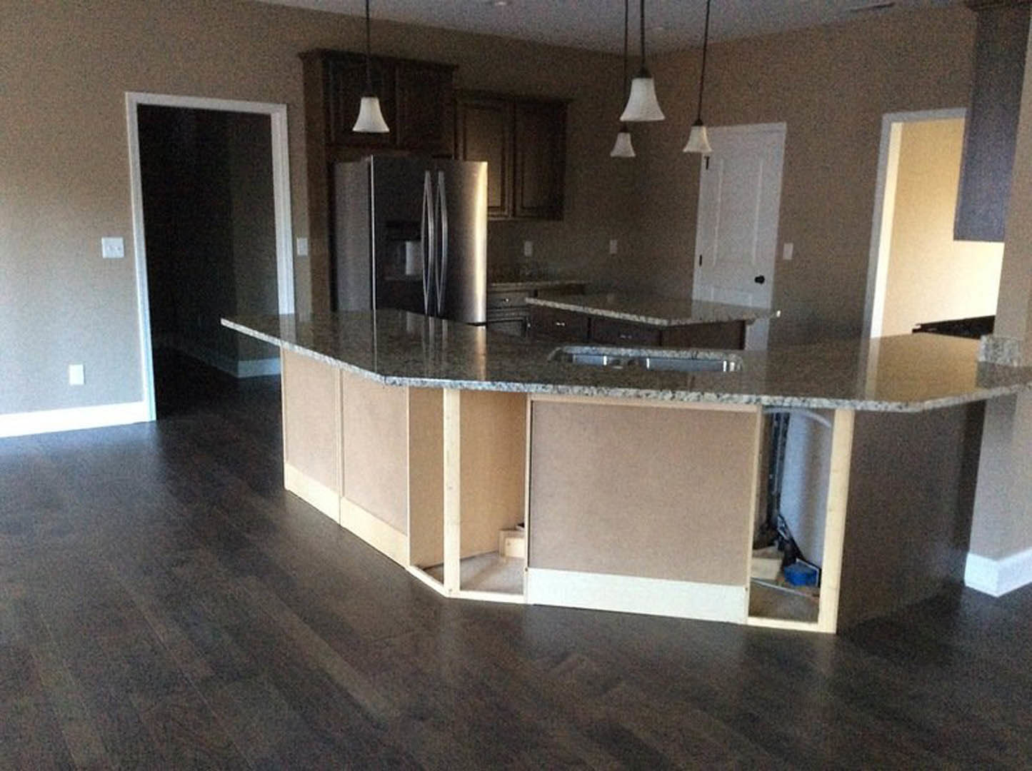 Modern kitchen featuring a large island with a built-in sink, sleek countertops, white cabinetry, stainless steel refrigerator, and pendant lighting against neutral walls and