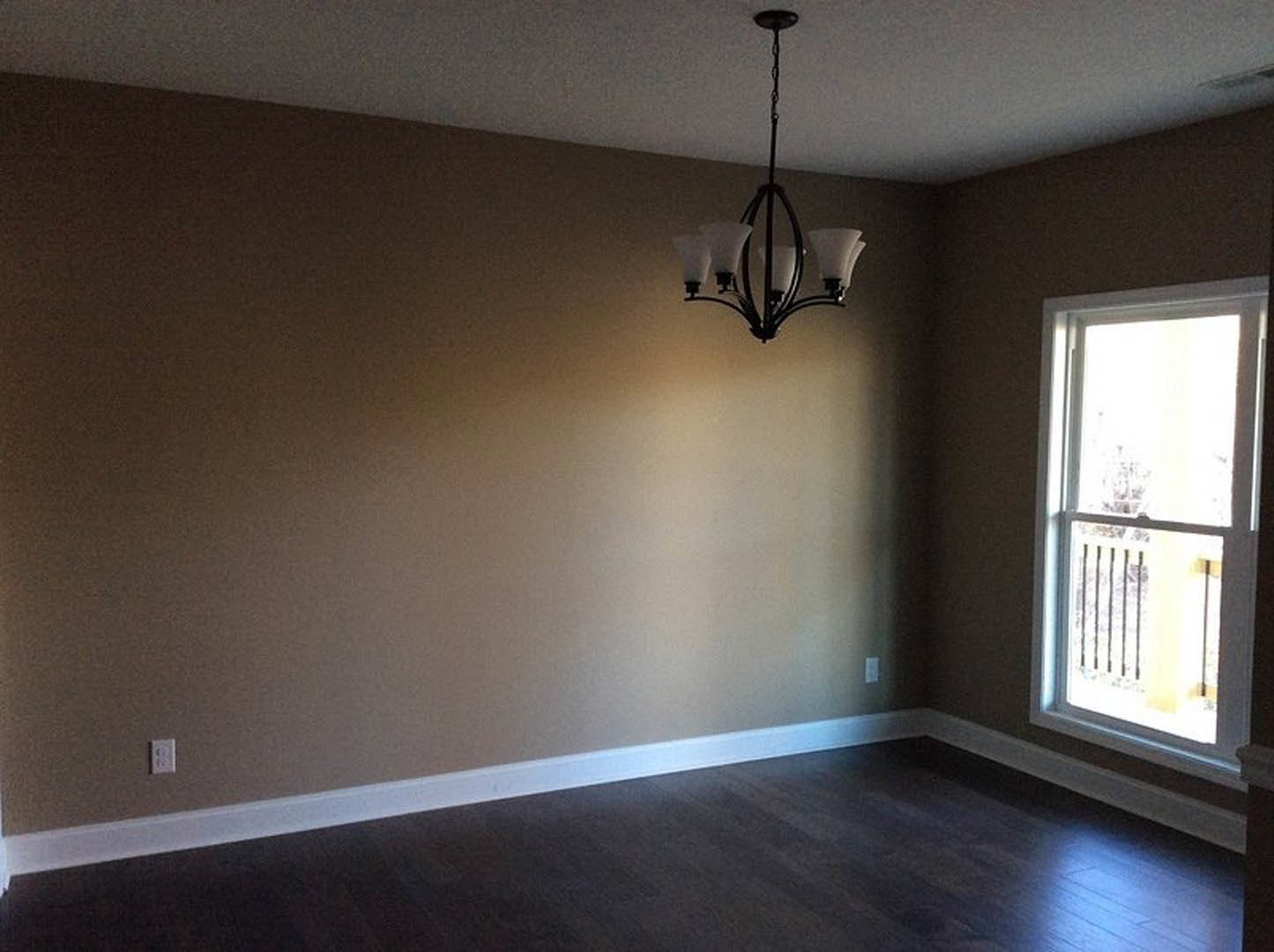 Chandelier hanging from plaster ceiling above wood laminate flooring, large window with decorative railing, tree visible outside
