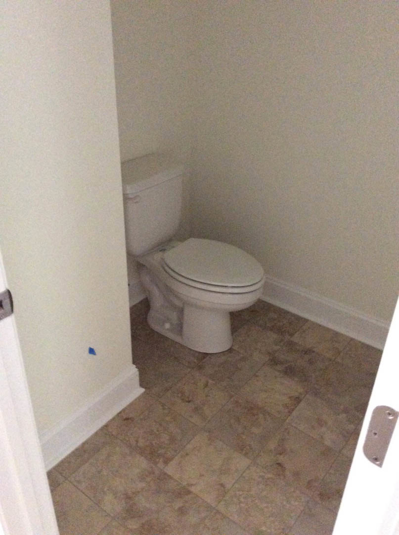 White toilet with lid up positioned in bathroom corner, surrounded by light-colored tile floor and wall.