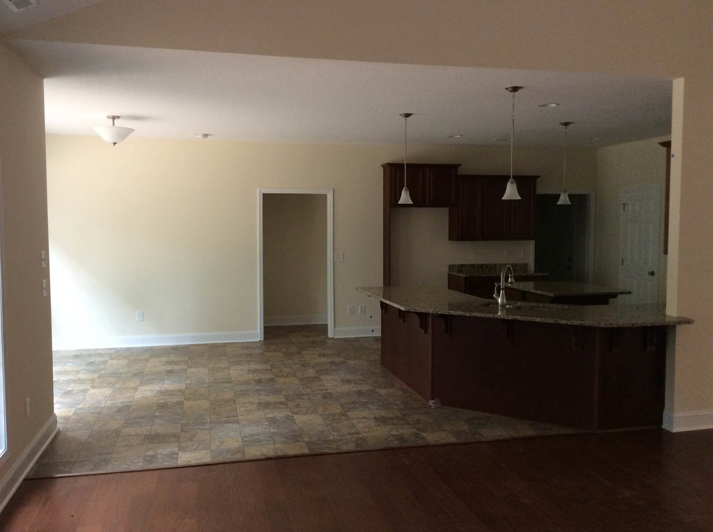 Open-concept kitchen and living room featuring light gray tile flooring, white cabinetry, stainless steel faucet, and a white door frame with matching trim.