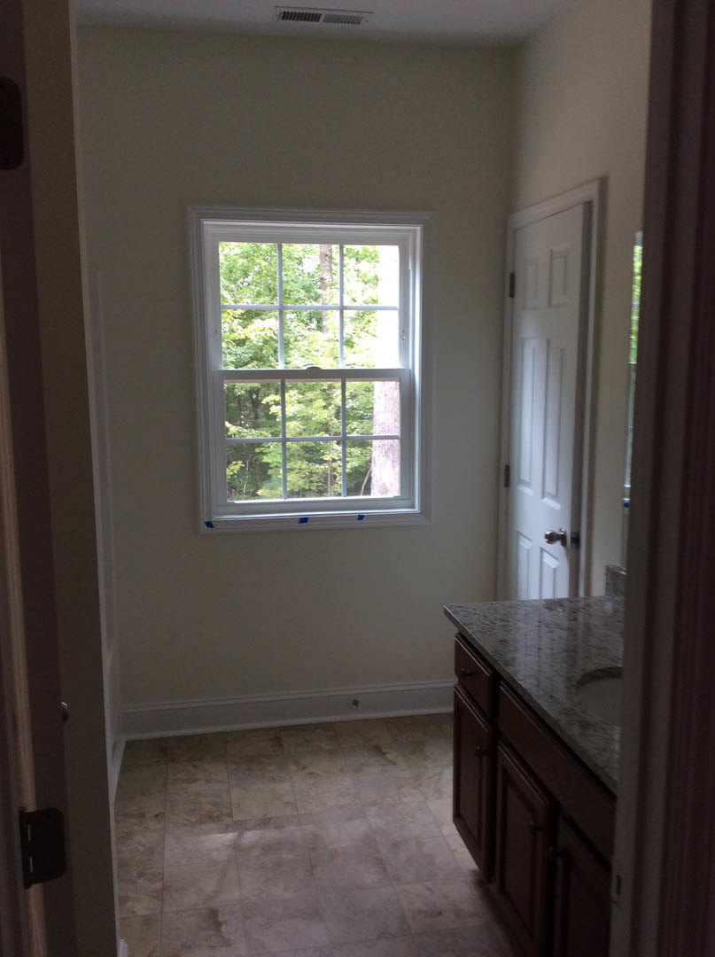 Bathroom with multi-pane window, white door, tile floor, white sink on stone countertop, dark rectangular fixture, cabinetry and drawers.
