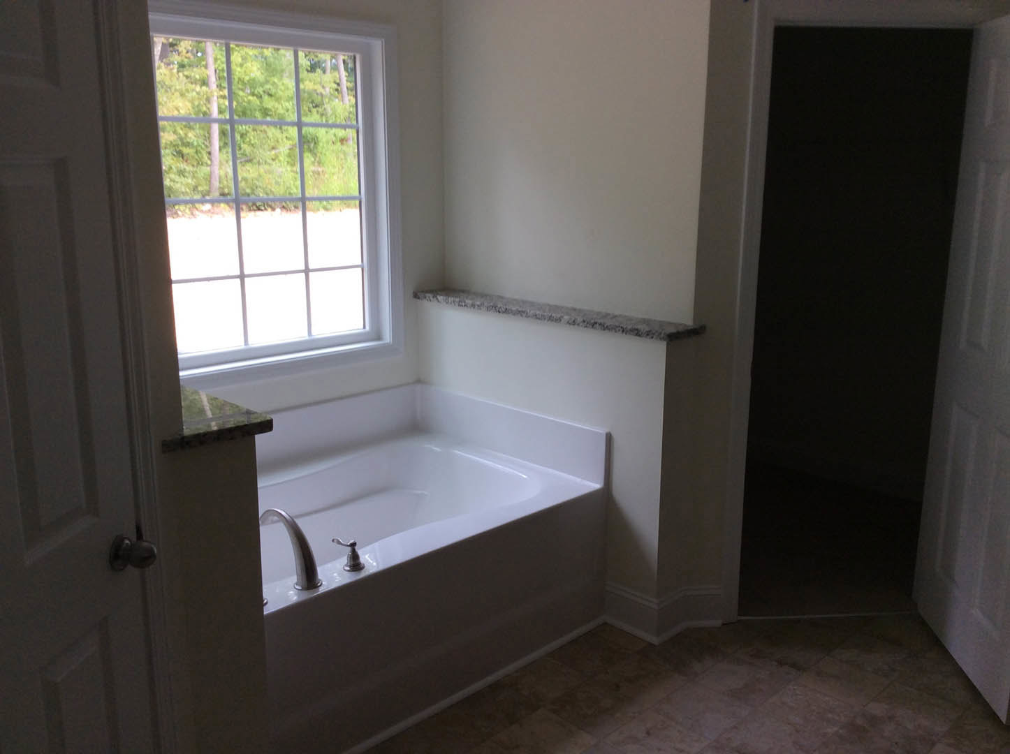 Freestanding white bathtub with chrome faucet beneath multi-pane window, white walls, light wood floor