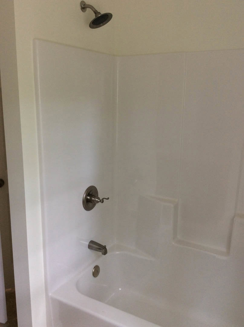White-tiled shower with chrome faucet and showerhead, adjacent to a built-in bathtub, bathroom wall visible in background