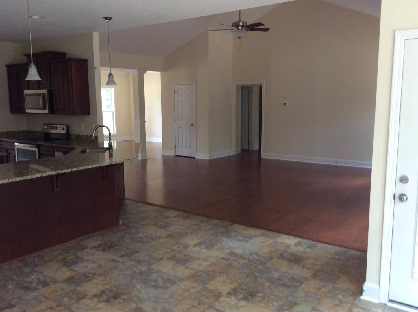 Open-concept kitchen and living room featuring granite countertops, wood and tile flooring, white cabinetry, stainless steel microwave with knob, white door with doorknob, ceiling