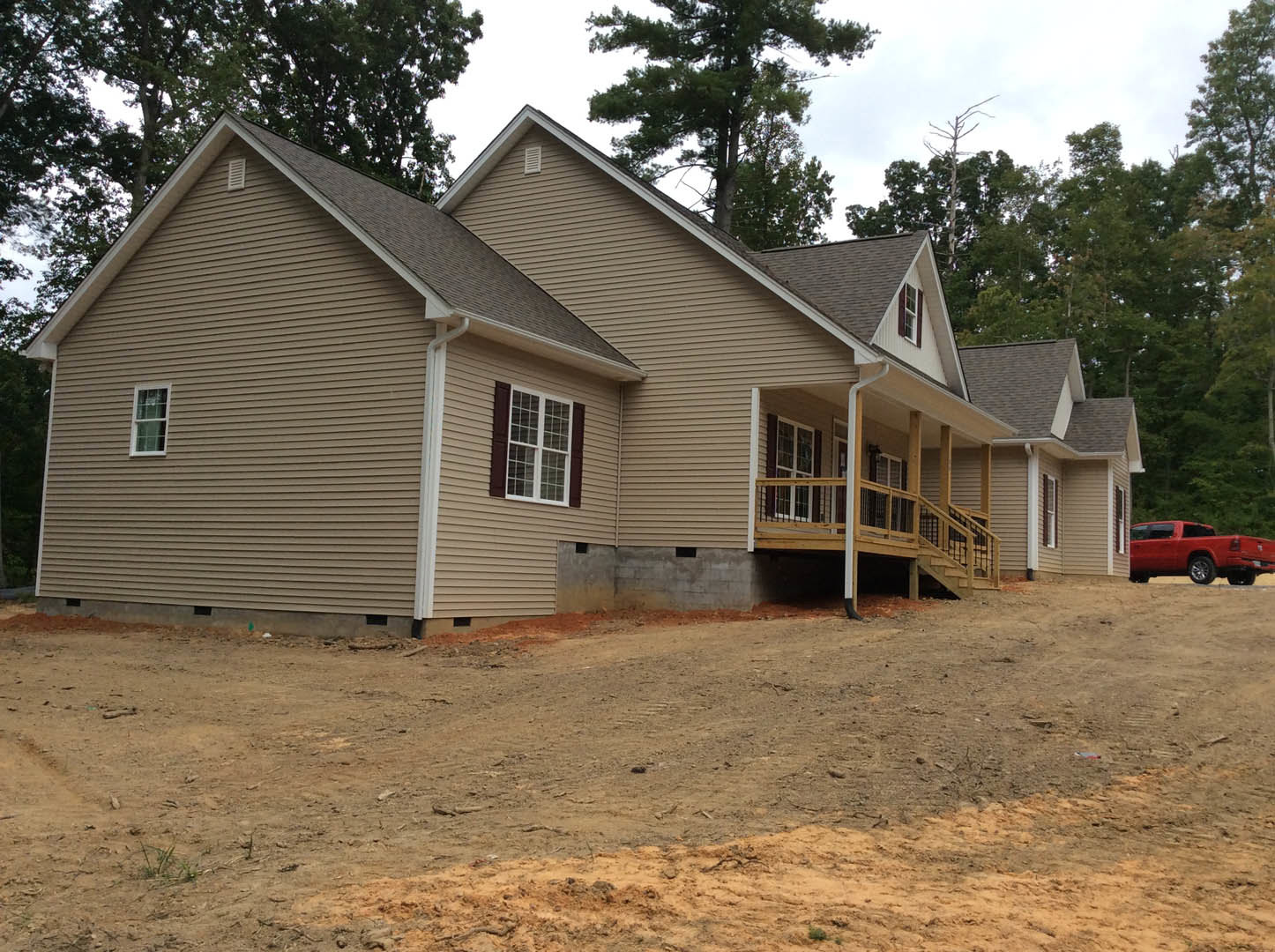 Two-story house with white siding, covered front porch, white-trimmed windows, dirt path leading to entrance, red truck parked on driveway, garage and trees in background