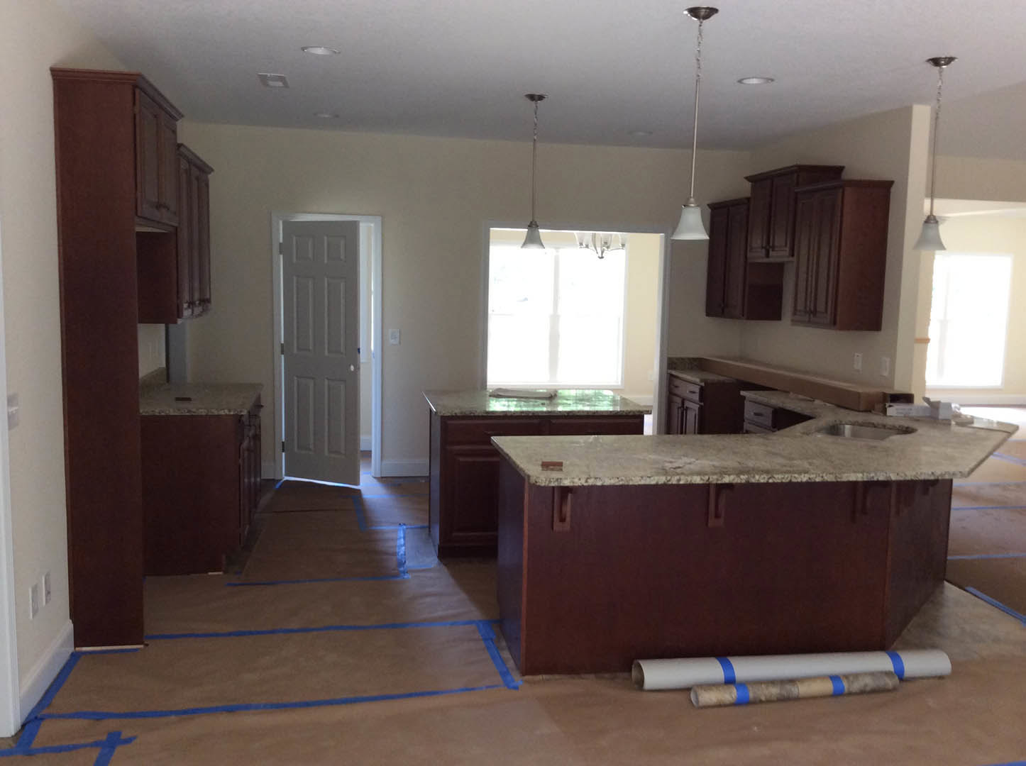 Marble kitchen countertop with undermount sink, white cabinetry, tile backsplash, and sunlight streaming through window onto light wood flooring
