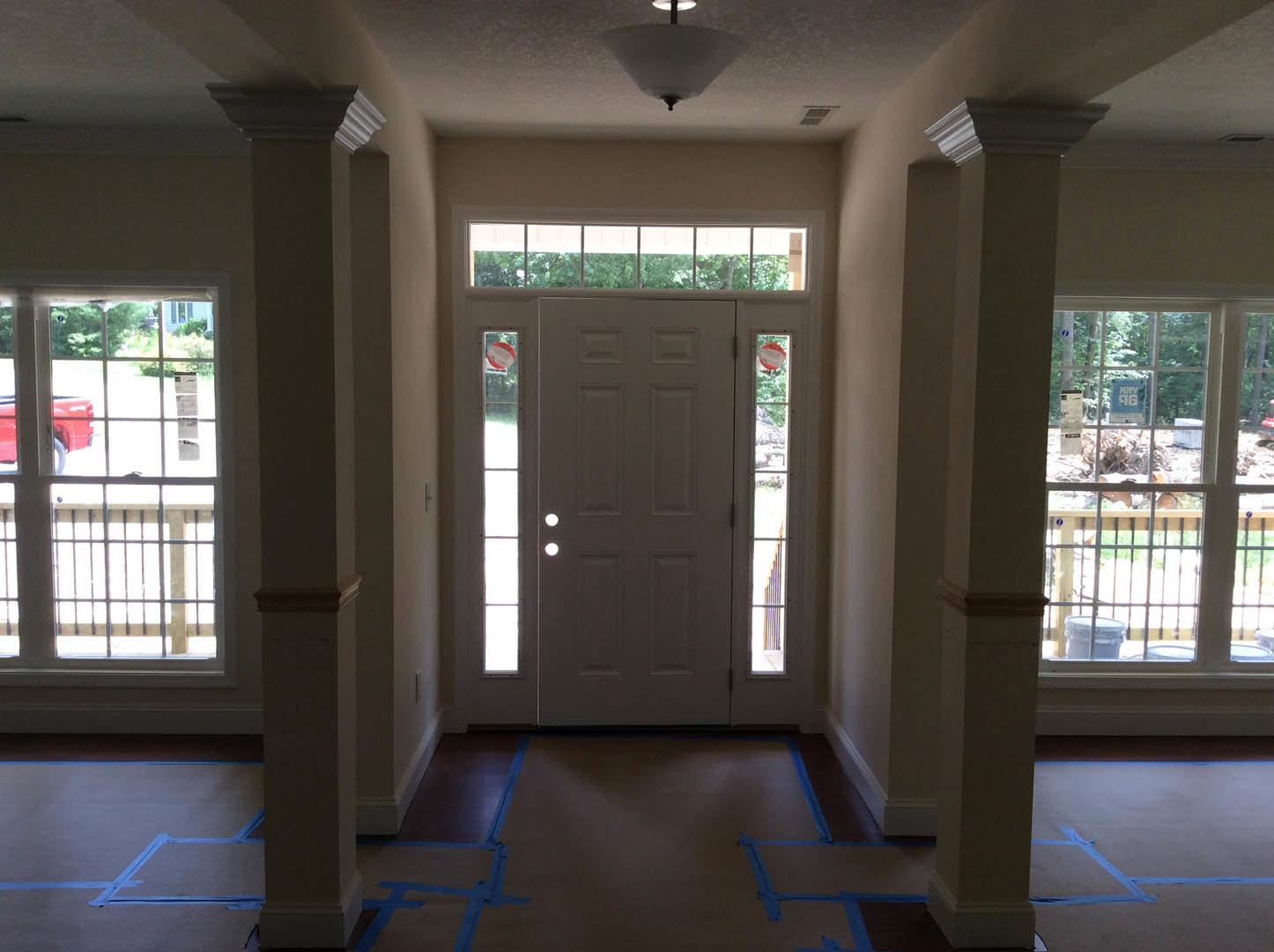 White paneled door with glass inserts in a hallway featuring light wood flooring, white walls, and a window with a white frame; red car visible outside through the window.