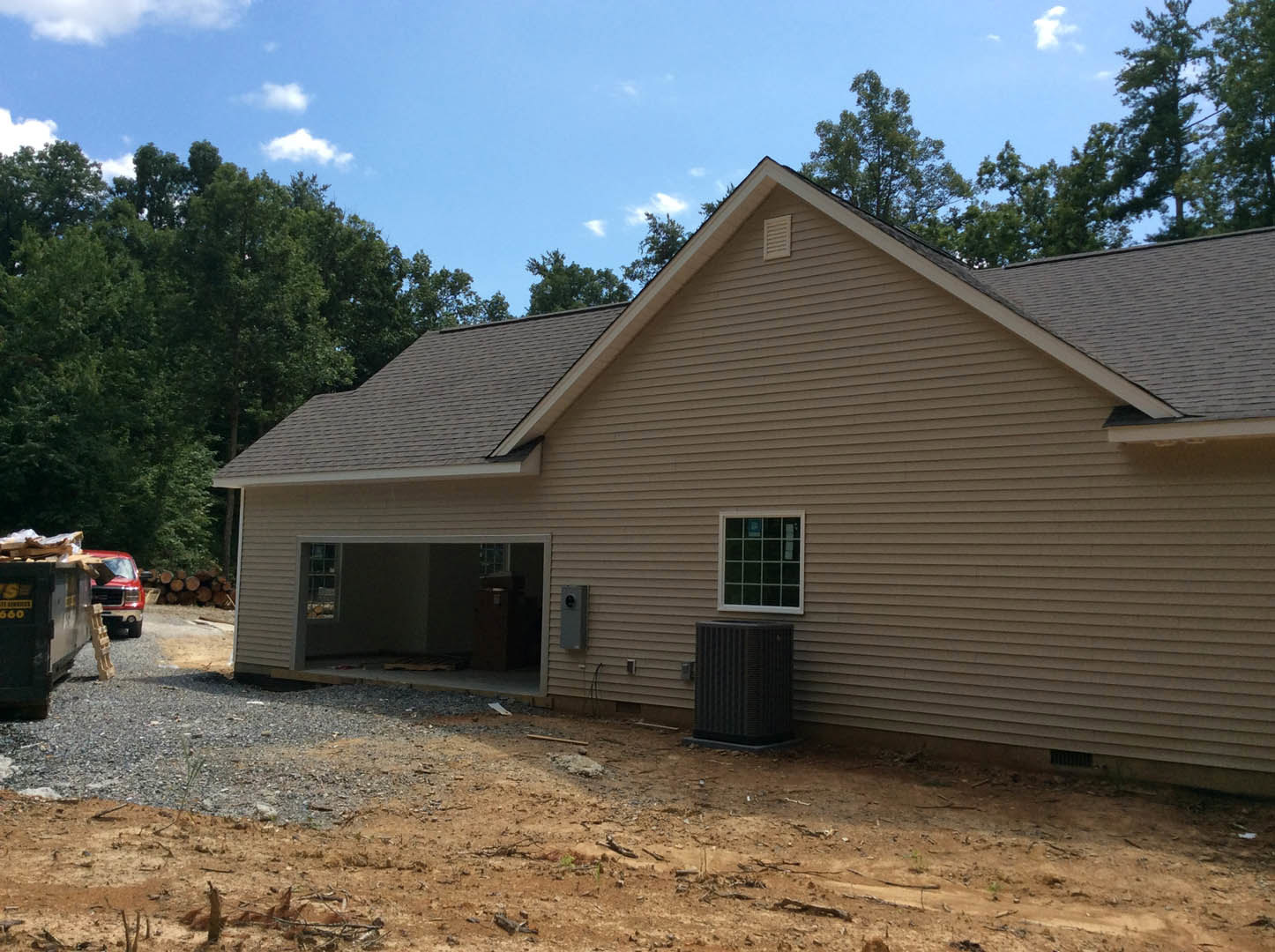 Two-story custom home with attached garage, multiple-pane windows, black metal waste container, pickup truck parked on dirt driveway, scattered construction debris, partly cloudy